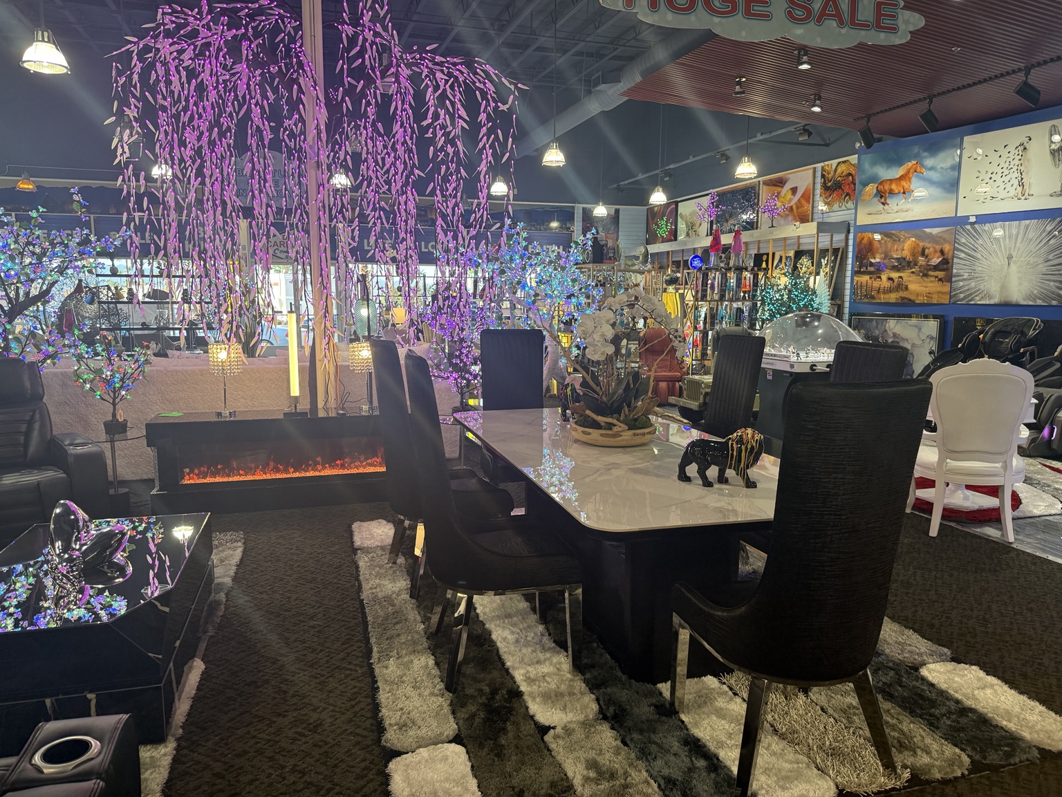 Dining table and chairs beside an illuminated fireplace, decorative trees, artwork, and collectibles inside HolySheets Galleria