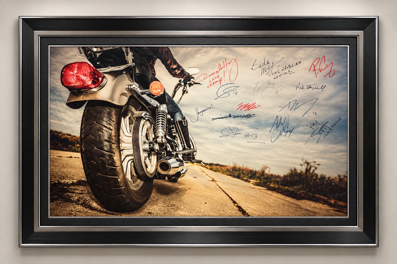 Framed motorcycle on an open road with handwritten signatures across the sky