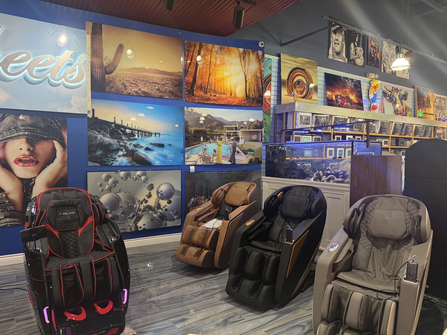 Four massage chairs arranged beside decorative wall art and a showroom aquarium inside HolySheets Galleria