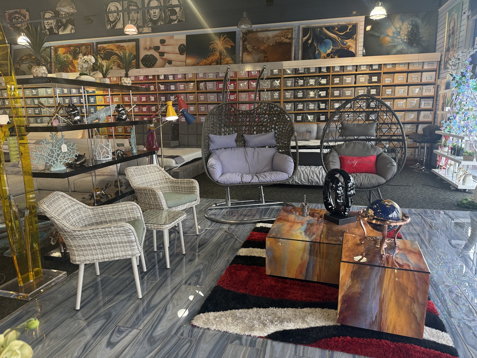 Two hanging chairs, woven accent chairs, sculptural tables, bedding, wall art, and decorative lighting inside HolySheets Galleria